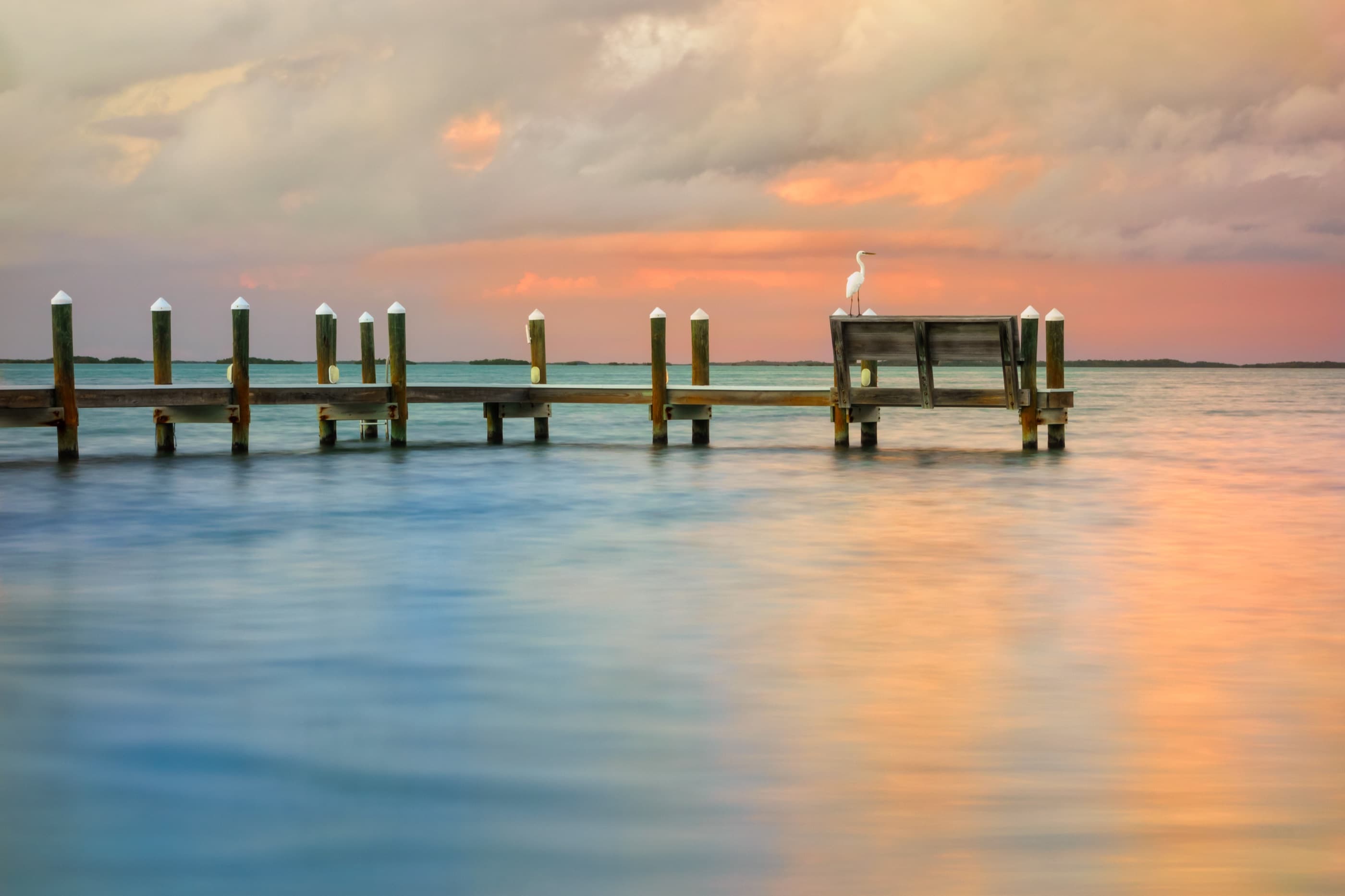 A wooden dock reaching into calm Florida Keys water at sunset